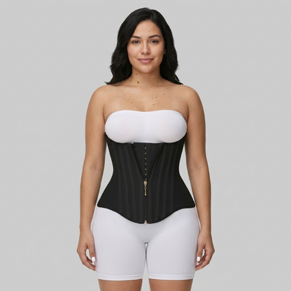 Woman wearing a black waist trainer over a white top and shorts on a gray background